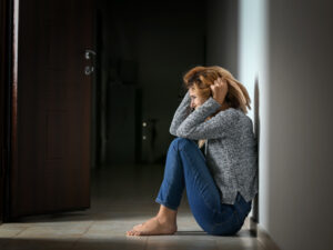 Distressed woman sitting on floor against wall, evoking themes of solitude and despair.