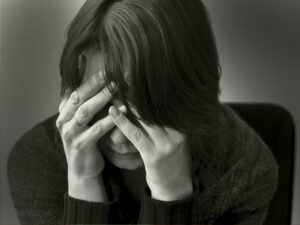 Monochrome image of a person with head in hands, showing signs of despair or headache.