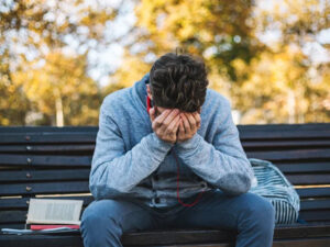 Man in distress sitting on a park bench, head in hands, with an open book beside him.