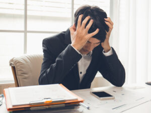 Businessman in distress with hands on head amidst work papers.