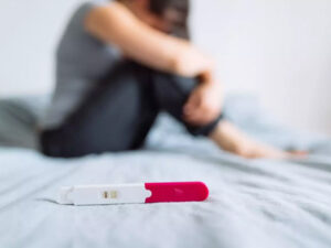 Focus on a positive pregnancy test on a bed, with a blurred figure in the background.