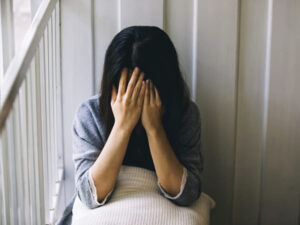 Woman sitting on stairs, covering her face with hands, in a gesture of distress.