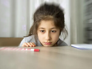 Pensive child at a table with a crayon, appearing distracted or tired.