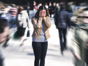 Woman covering her face with hands, standing still amidst a blurry crowd.