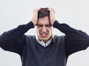 Alt text: "Man in distress holding his head, showing signs of a headache or stress.