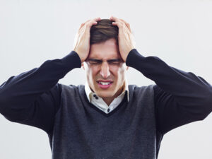 Alt text: "Man in distress holding his head, showing signs of a headache or stress.