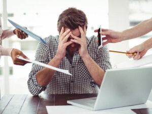 Overwhelmed man at desk surrounded by hands holding office items.